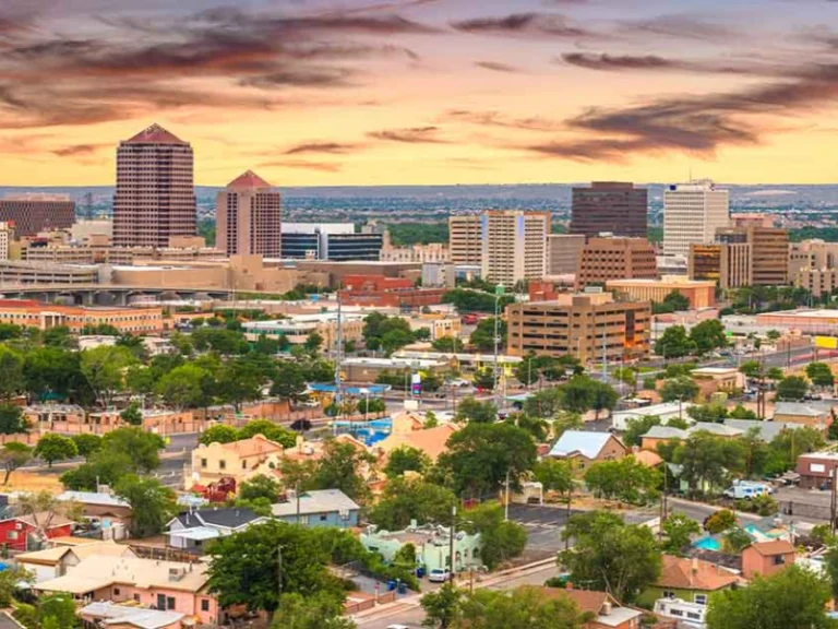 City skyline with tall buildings and residential houses under a colorful sunset sky. water damage restoration in Albuquerque