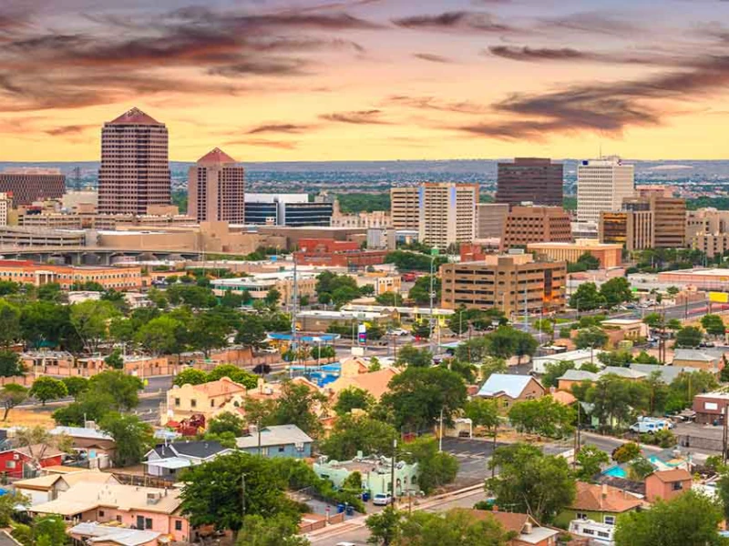 City skyline with tall buildings and residential houses under a colorful sunset sky. water damage restoration in Albuquerque
