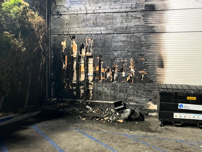 Charred exterior wall with fire damage and burnt debris near a dumpster in a parking lot. fire damage restoration company