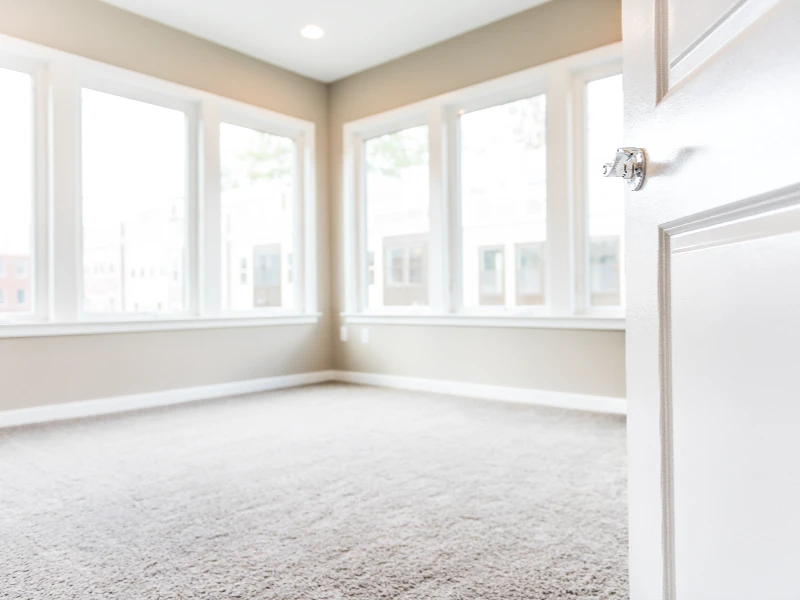 Empty room with beige walls, carpeted floor, and multiple large windows letting in natural light. tenant trash out service