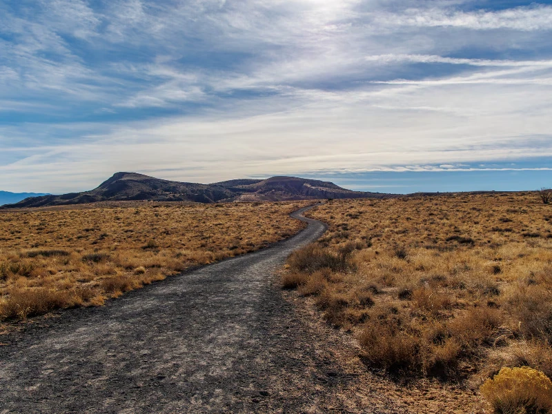 Winding dirt path through dry grassland with low hills under a partly cloudy sky. water damage restoration Los Lunas