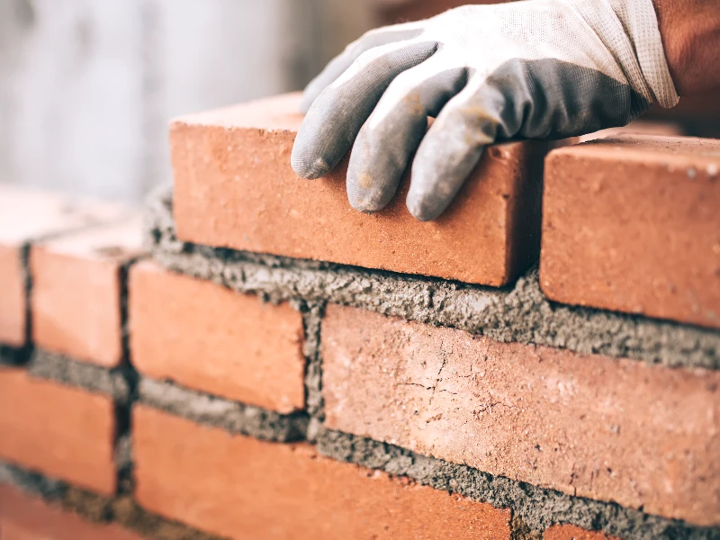 Hand in glove placing a brick on a partially built brick wall with mortar. disaster reconstruction services