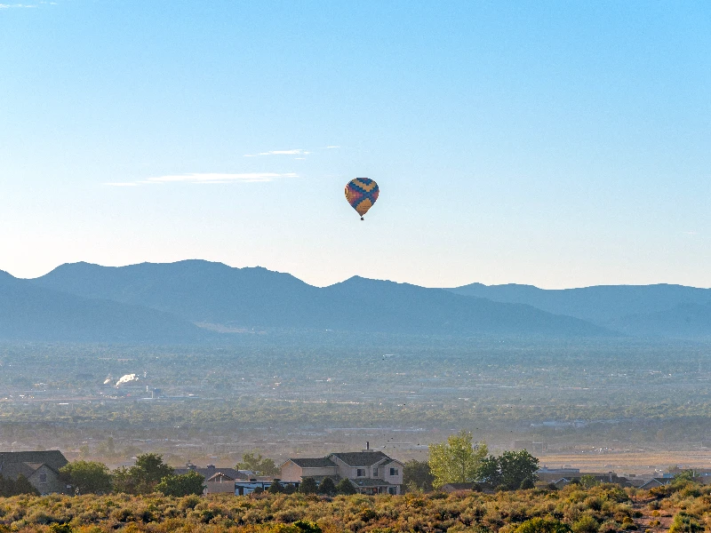 A colorful hot air balloon floats above a suburban area with mountains in the background. water damage restoration Rio Rancho