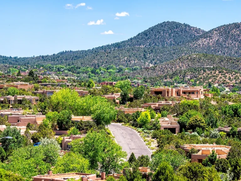 Residential neighborhood with adobe-style houses surrounded by green trees and hills in the background. water damage restoration Santa Fe
