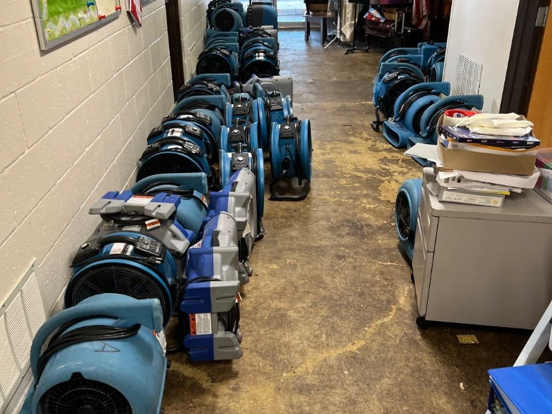 Multiple blue industrial air movers from a damage restoration company lined up along a hallway floor.